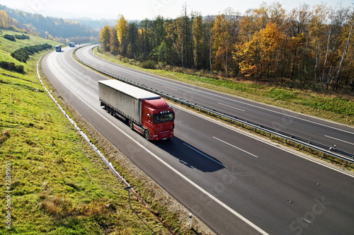 Obraz na płótnie The highway between forests in fall colors, three trucks w salonie