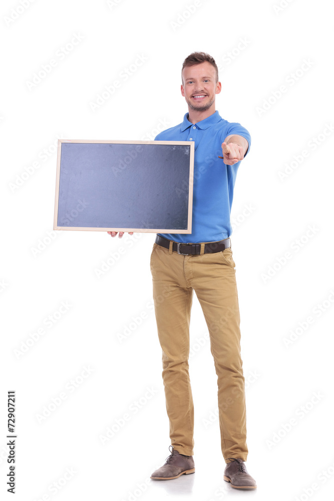 casual young man holds blackboard and points at you casual young man holds blackboard and points at you