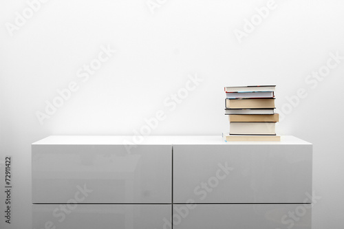 Foto white commode with stack of books in bright minimalism interior