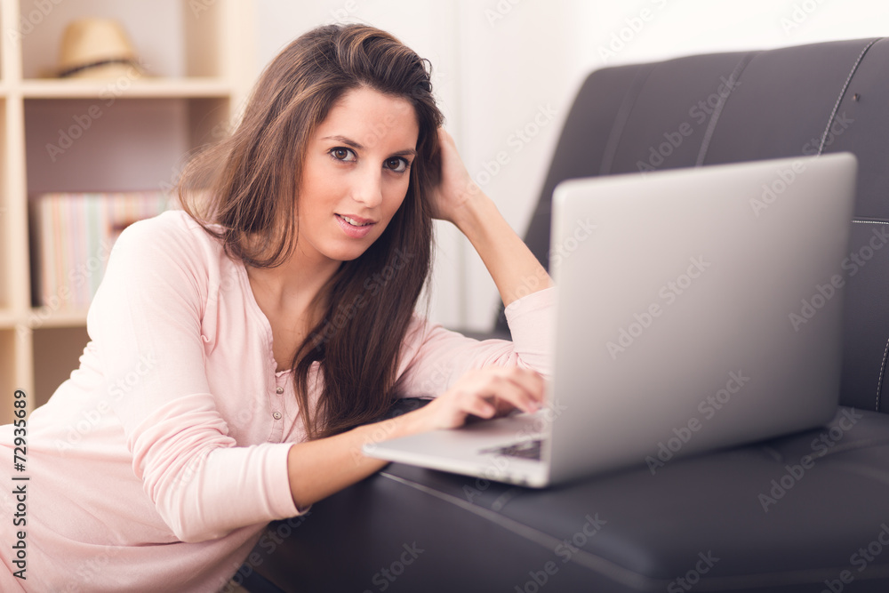 Fototapeta premium Smiling young woman looking on your laptop sitting on floor at h