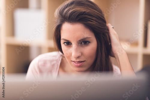 Smiling young woman looking on your laptop sitting on floor at h