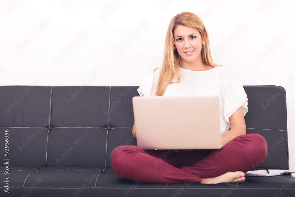 Smiling young woman looking on your laptop sitting on sofa at ho Smiling young woman looking on your laptop sitting on sofa at ho