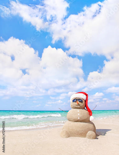 Smiling sandy snowman in red santa hat on the sea beach