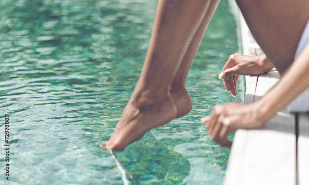 Young Woman Sitting at Poolside with Toes on Water