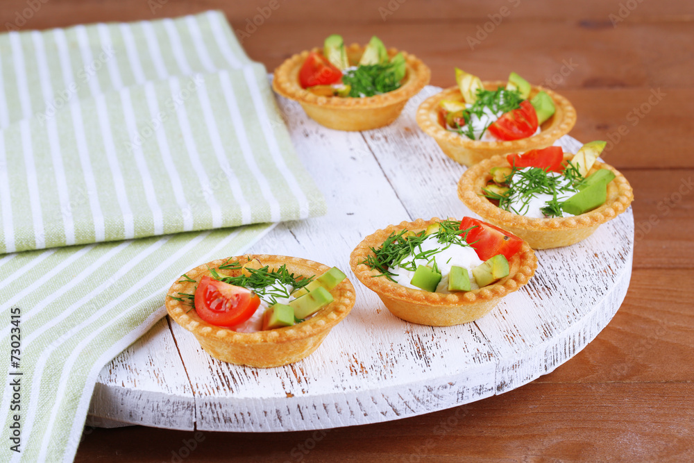 Tartlets with greens and vegetables with sauce on tray on table