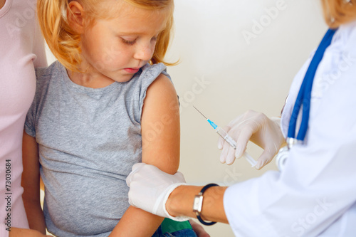 Doctor vaccinating small redhead girl.