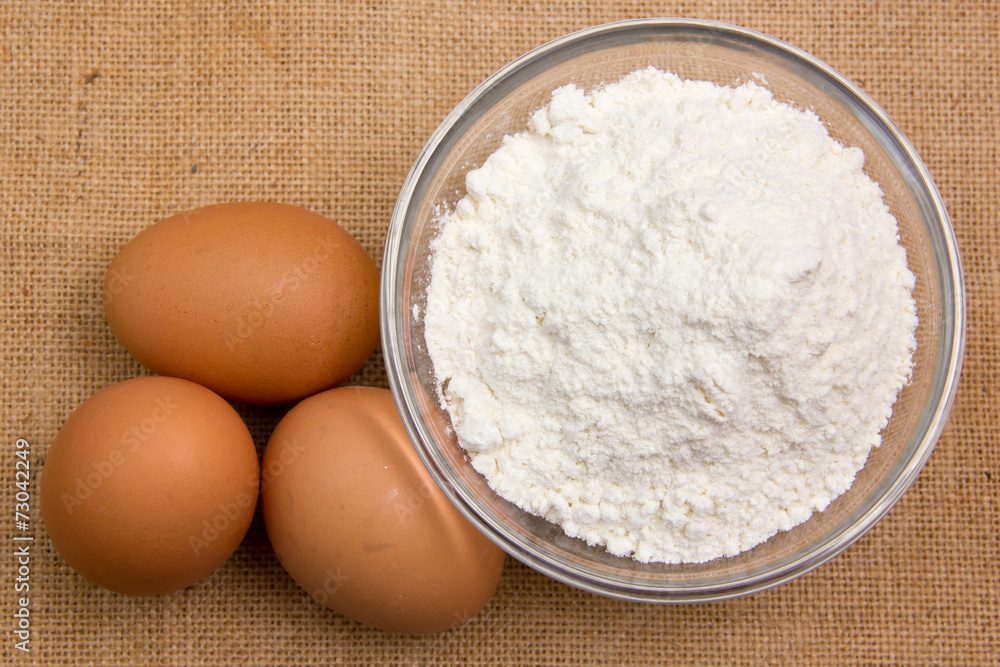Eggs and flour in bowl on jute tablecloth viewed from above Eggs and flour in bowl on jute tablecloth viewed from above
