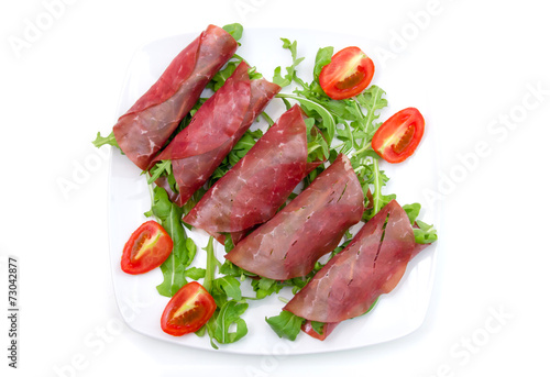 Rolls of dried beef on plate on white background seen from above