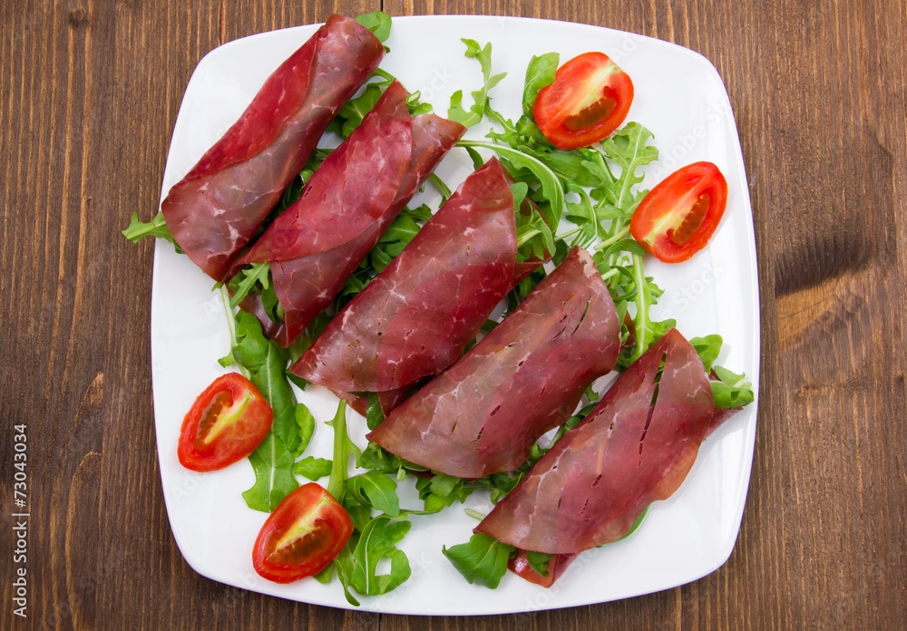 Rolls of dried beef on plate over wooden table seen from above Rolls of dried beef on plate over wooden table seen from above