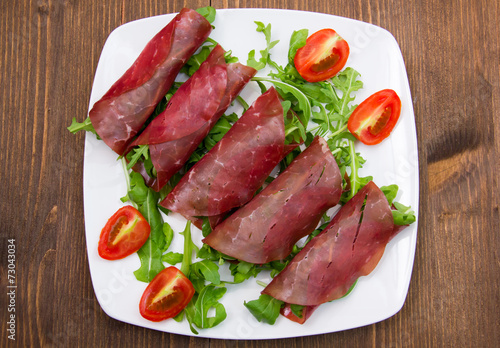 Rolls of dried beef on plate over wooden table seen from above