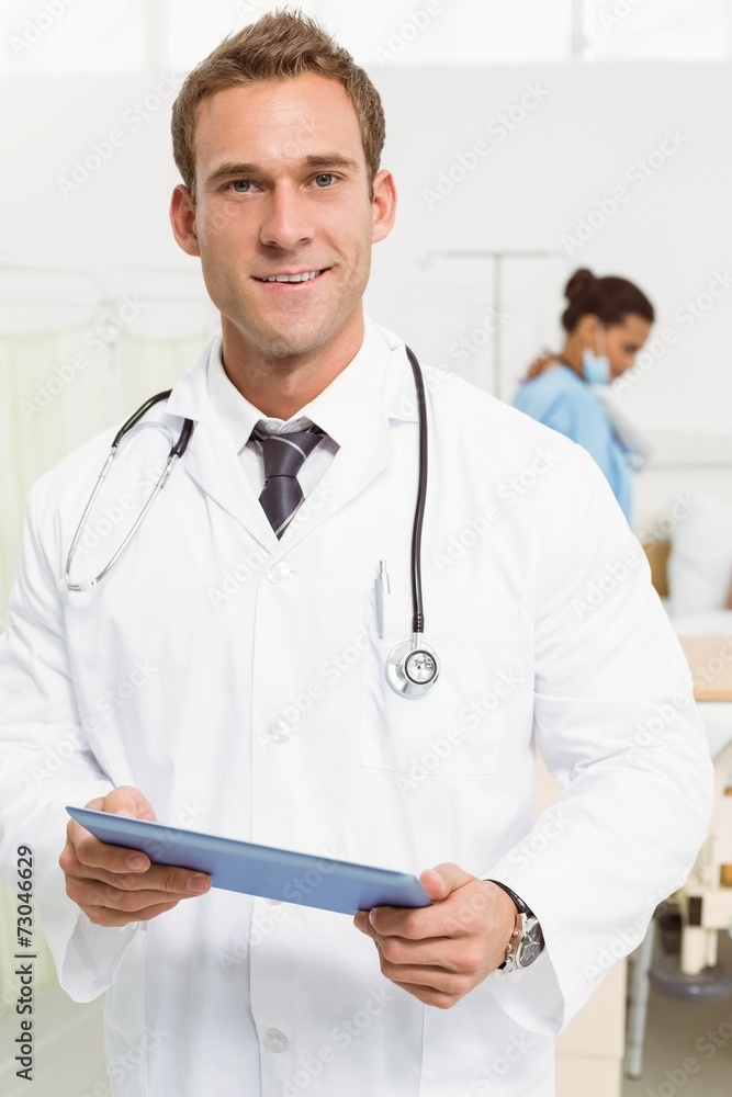 Doctor using digital tablet with colleagues and patient behind Doctor using digital tablet with colleagues and patient behind