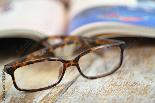 Reading glasses and open book on rustic wooden surface