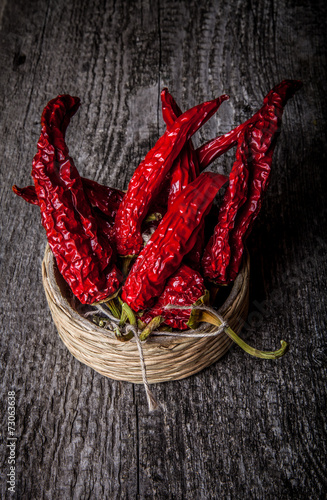 bunch of red hot peppers lying in a wicker basket on old wooden