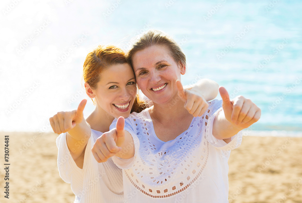 Fototapeta premium Joyful mother daughter showing thumbs up having fun on beach