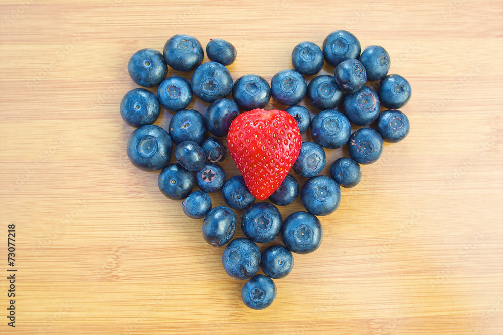 Heart made of blueberries with strawberry in centre Heart made of blueberries with strawberry in centre
