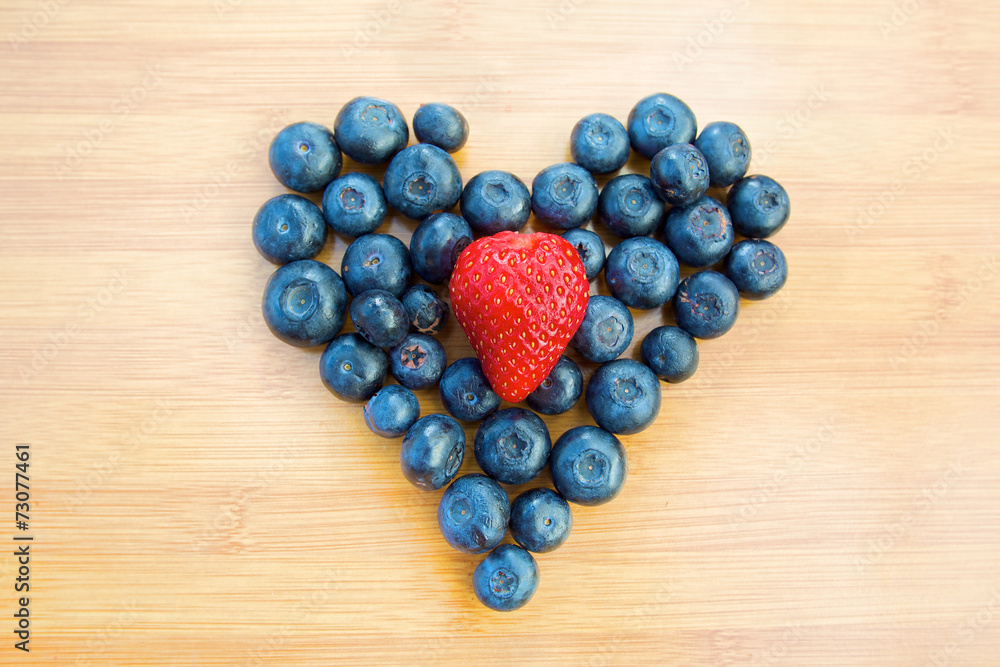 Heart made of blueberries with strawberry in centre Heart made of blueberries with strawberry in centre