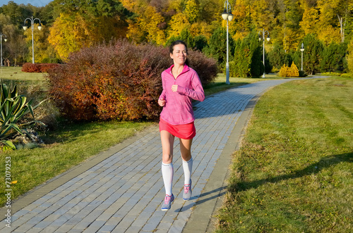 Woman running in autumn park, beautiful girl runner jogging