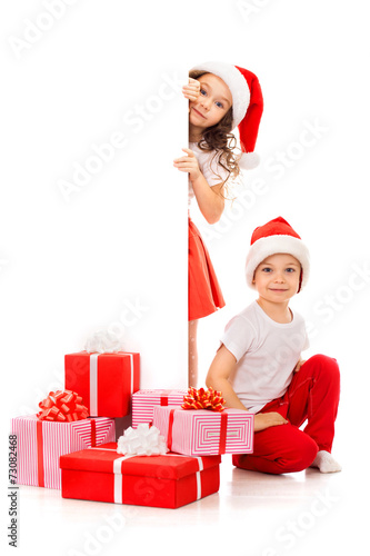 Happy little kids in Santa hat peeking from behind blank sign