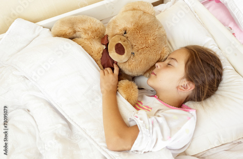 little brunette girl sleeping in bed with teddy bear