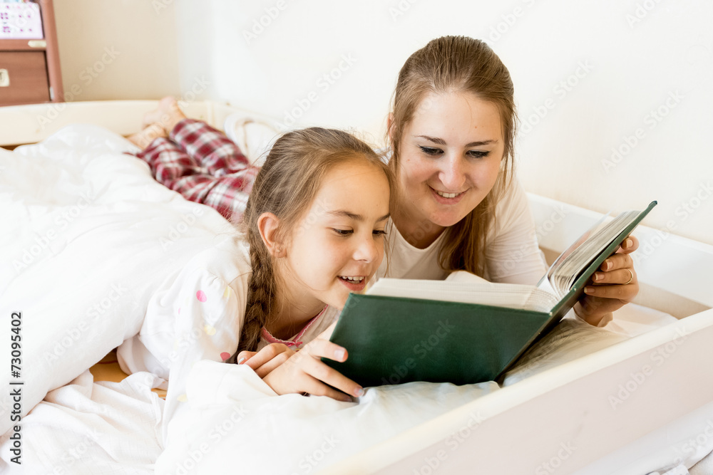 portrait of mother lying with daughter on bed and reading book portrait of mother lying with daughter on bed and reading book