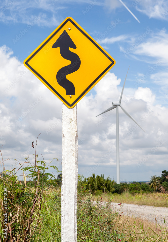 Winding road sign with windmill background in wind farm.