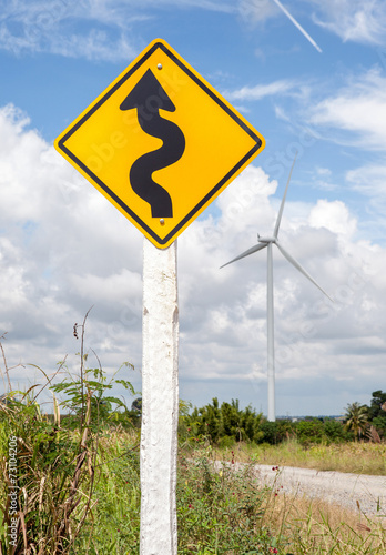 Winding road sign with windmill background in wind farm.