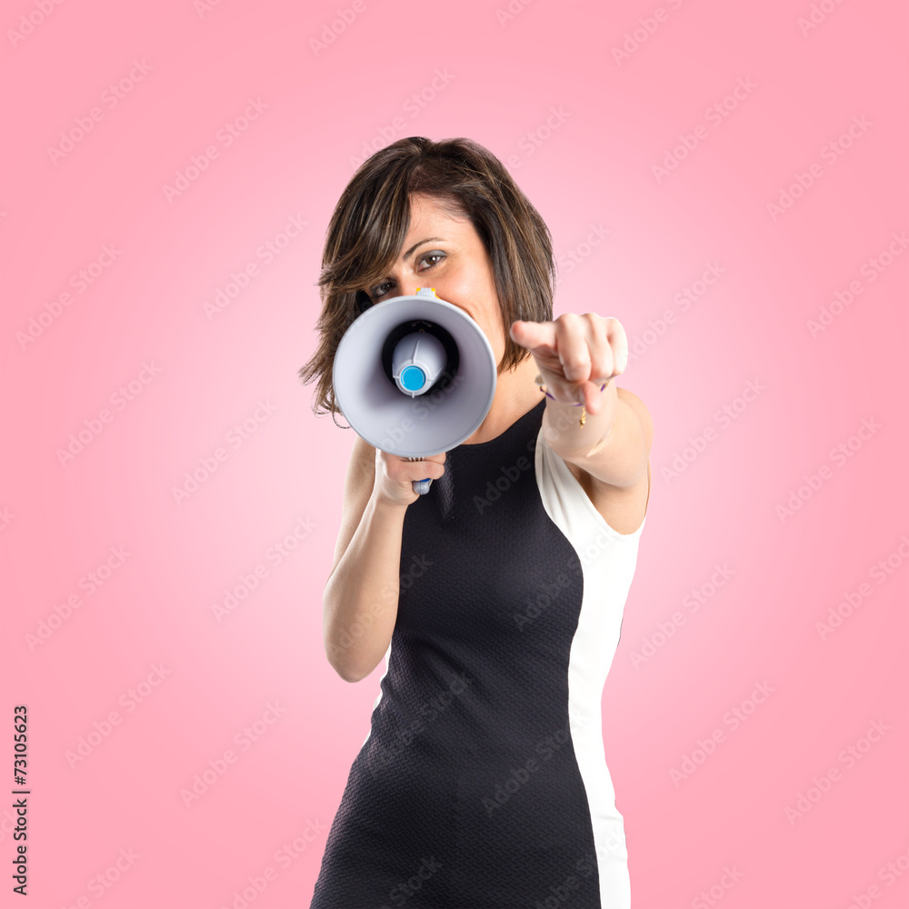 Fototapeta premium Pretty girl shouting with a megaphone over pink background