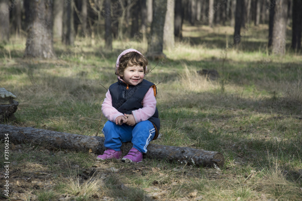 In the spring of a little girl sitting on a log in the forest. In the spring of a little girl sitting on a log in the forest.