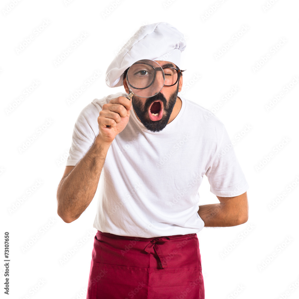 Chef with magnifying glass over white background Chef with magnifying glass over white background