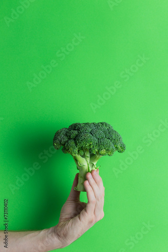 Hand holding broccoli on green background