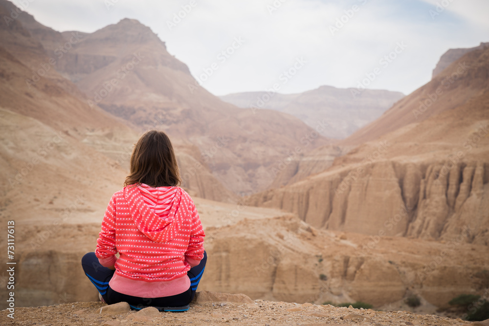 Woman sitting desert mountain edge above canyon