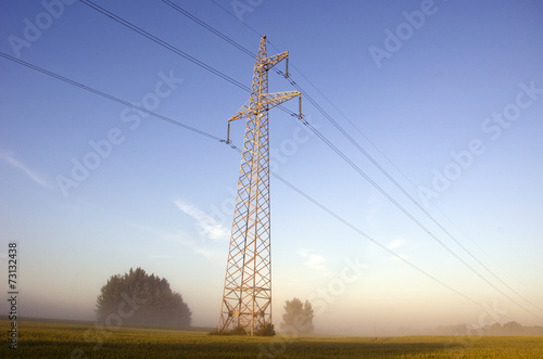 high voltage post.High-voltage tower on farm field in mist