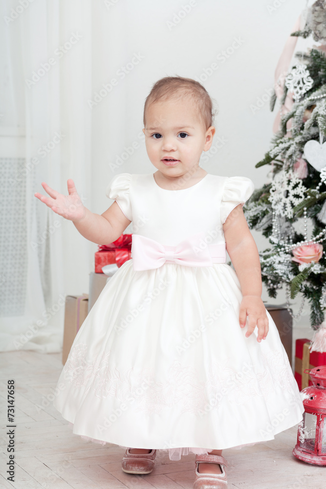 Little girl in a white dress stand near a Christmas fir-tree Little girl in a white dress stand near a Christmas fir-tree
