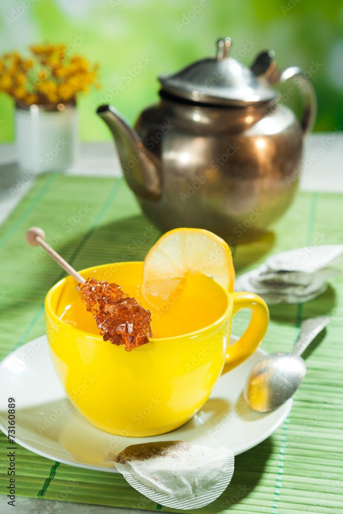 cup of tea with sugar candy and a kettle in the background cup of tea with sugar candy and a kettle in the background