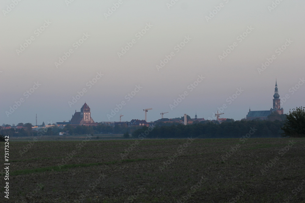 Fototapeta premium Meadows with misty view on the city of Greifswald, Mecklenburg-Vorpommern, Germany