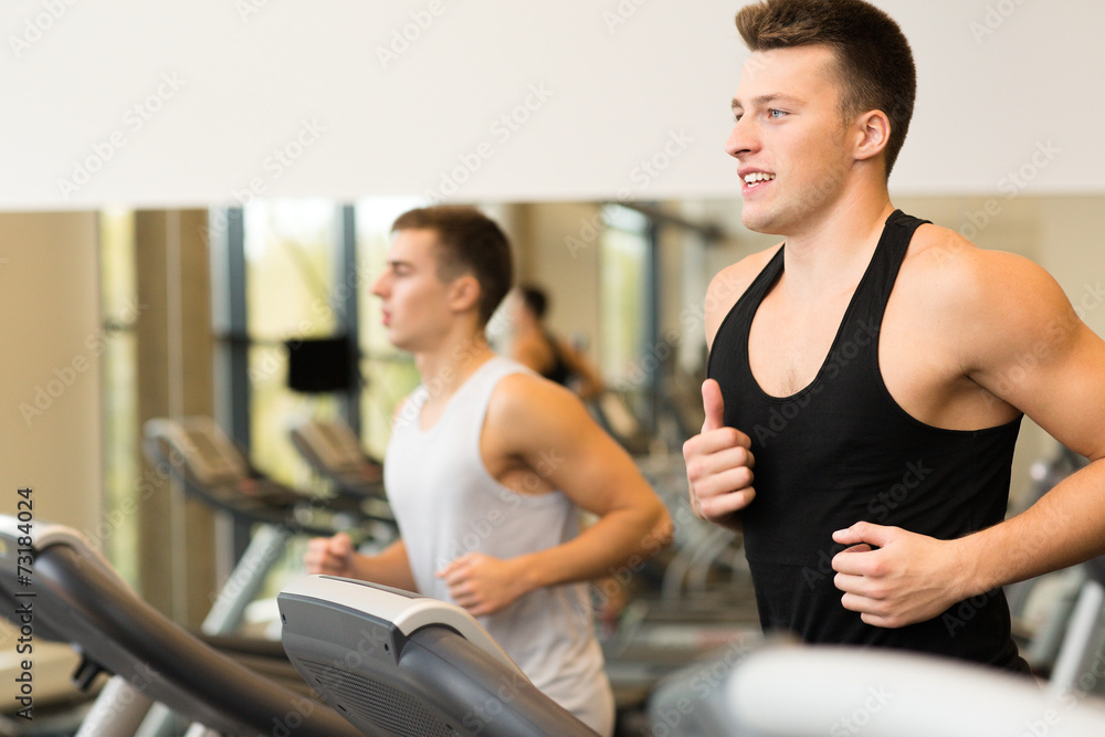 smiling men exercising on treadmill in gym