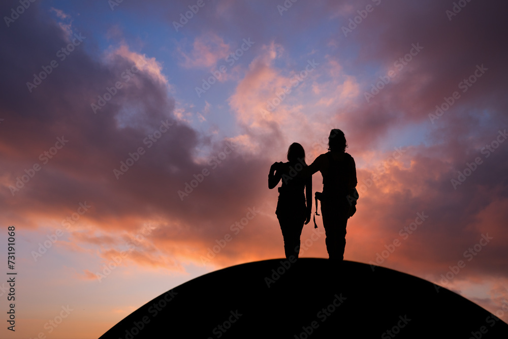 silhouetted couple standing on hill in sunset sky silhouetted couple standing on hill in sunset sky