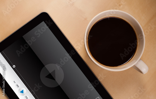 Tablet pc showing media player on screen with a cup of coffee on