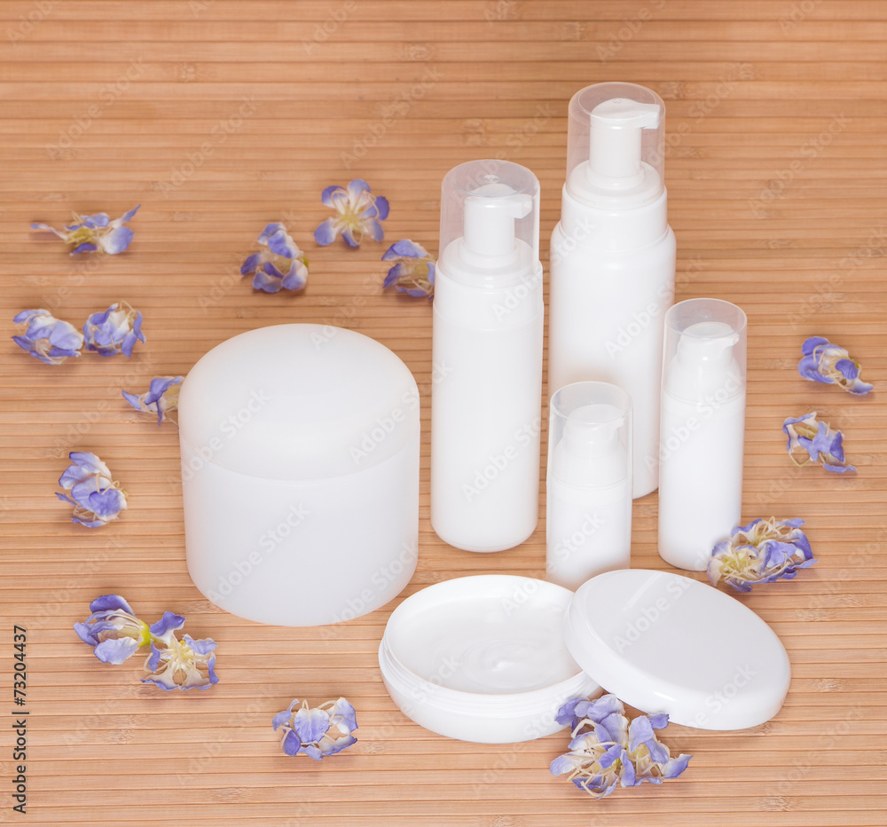 Open jar of cream and other body care cosmetics with flowers