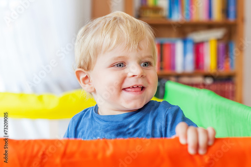 Cute little baby boy playing in colorful playpen, indoors