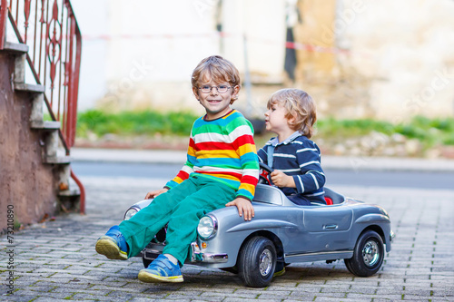 Two happy kids playing with big old toy car in summer garden, ou © Irina Schmidt