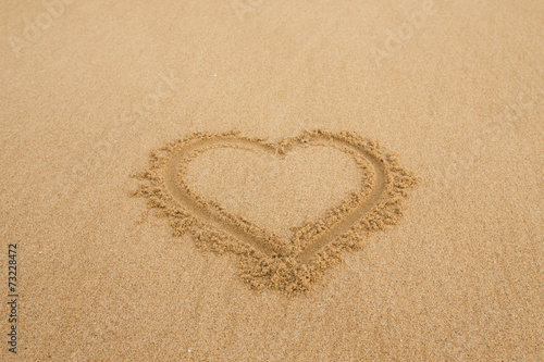 drawing a heart on wet golden beach sand