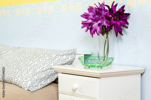 Кровать с тумбочкой. Декоративные цветы. Голубые и желтые обои