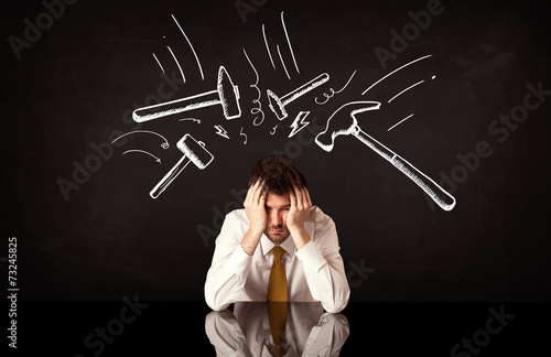 Depressed businessman sitting under hammer marks photo