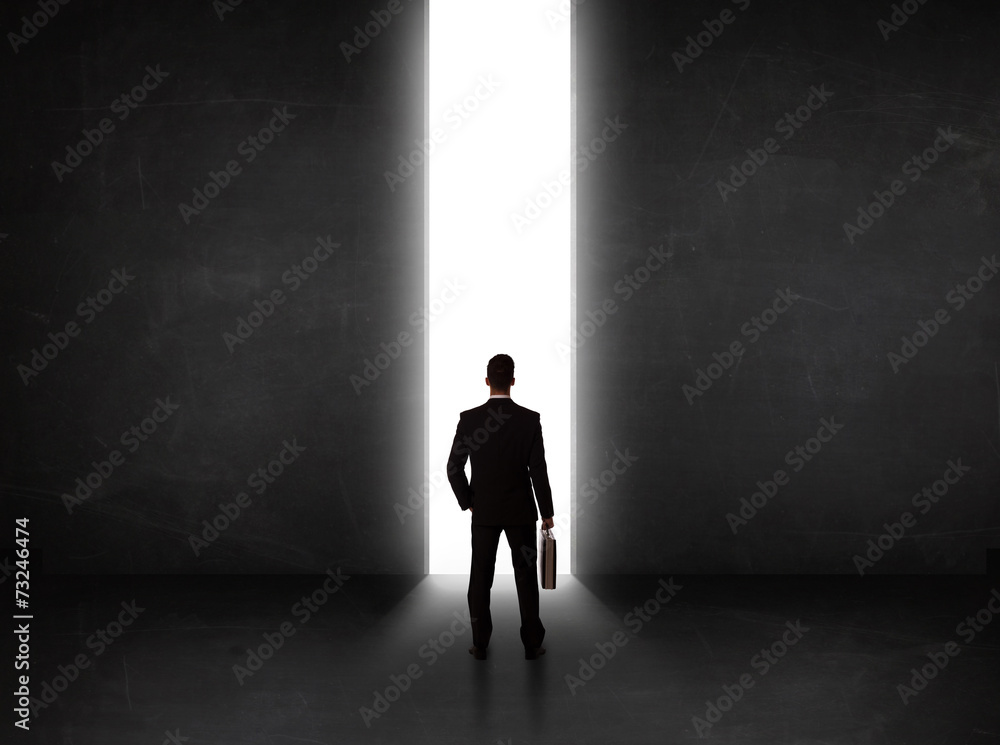 Business person looking at wall with light tunnel opening Business person looking at wall with light tunnel opening