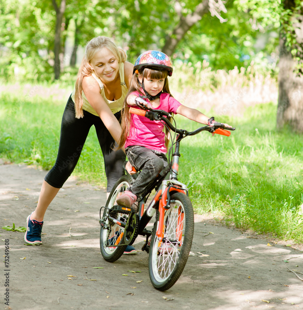 happy mother teaches his daughter to ride a bike