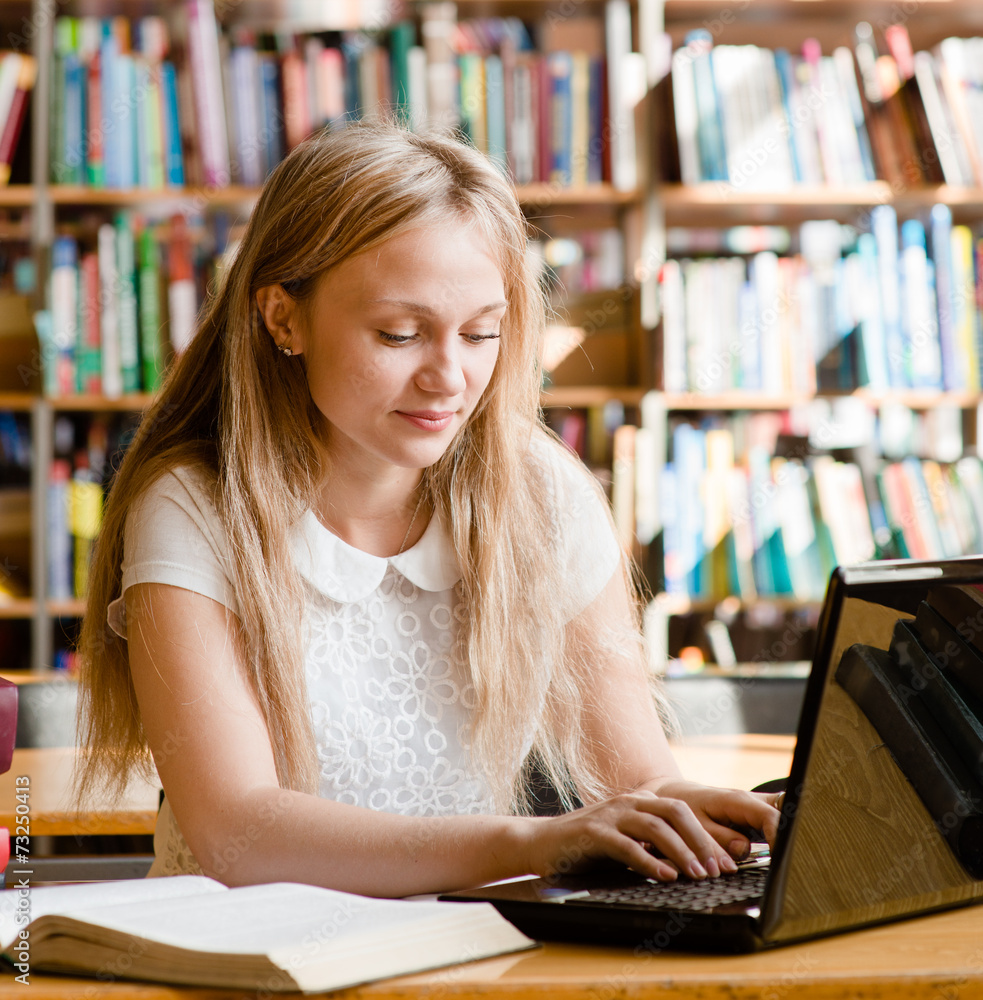pretty female student typing on notebook in library pretty female student typing on notebook in library