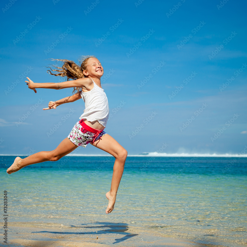 Naklejka premium teen girl jumping on the beach at blue sea shore in summer vaca