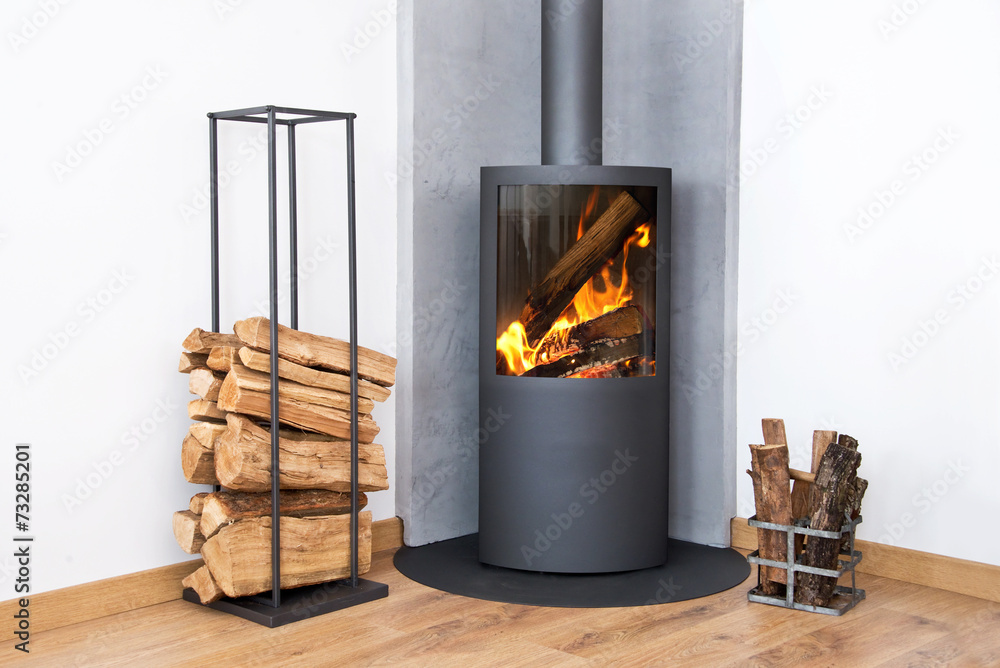 Fototapeta premium Photo of a fire in a modern burning stove next to a wood logs rack, contemporary home log burner or fireplace, renewable energy heating in winter