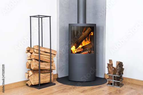 Slika na platnu Modern burning stove next to a wood logs rack